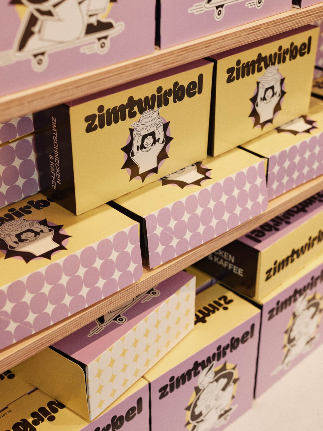 Zimtwirbel Verpackungsdesign: gestapelte Boxen in Lila und Gelb als Teil des Bäckerei Brandings für Zimtschnecken und Kaffee