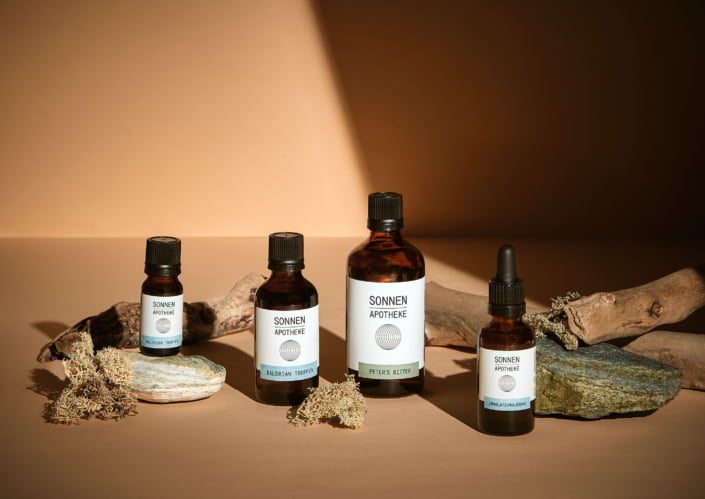 Sonnenapotheke Mieming Apotheke Verpackungsdesign: vier Apothekenflaschen mit Baldrian Tropfen, Peter's Bitter und Inhalationslösung auf Natursteinen