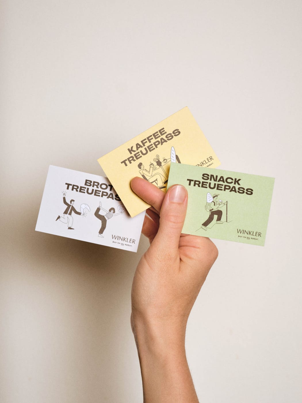 Bäckerei Branding der Bäckerei Winkler: Hand hält farbige Treuepässe für Brot, Kaffee und Snacks mit individuellen Illustrationen und modernem Corporate Design