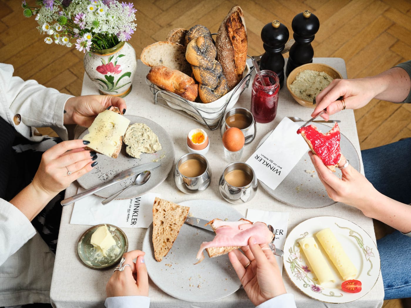 Bäckerei Winkler Frühstückstisch mit Gebäck und Händen die Besteck halten und Servietten mit Bäckerei Branding für Bäckerei Winkler