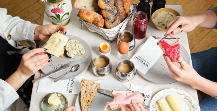 Bäckerei Winkler Frühstückstisch mit Gebäck und Händen die Besteck halten und Servietten mit Bäckerei Branding für Bäckerei Winkler