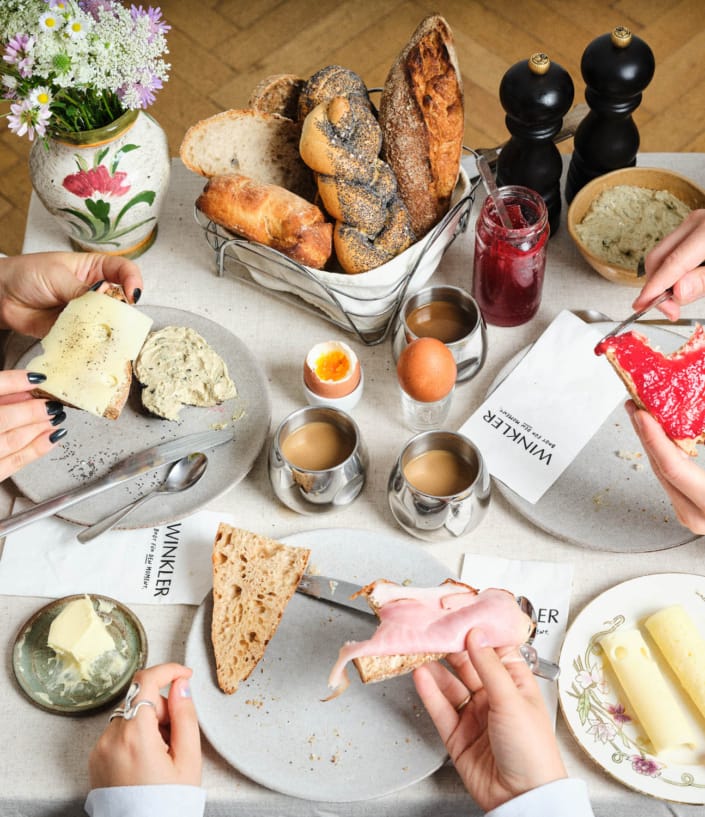 Bäckerei Winkler Frühstückstisch mit Gebäck und Händen die Besteck halten.