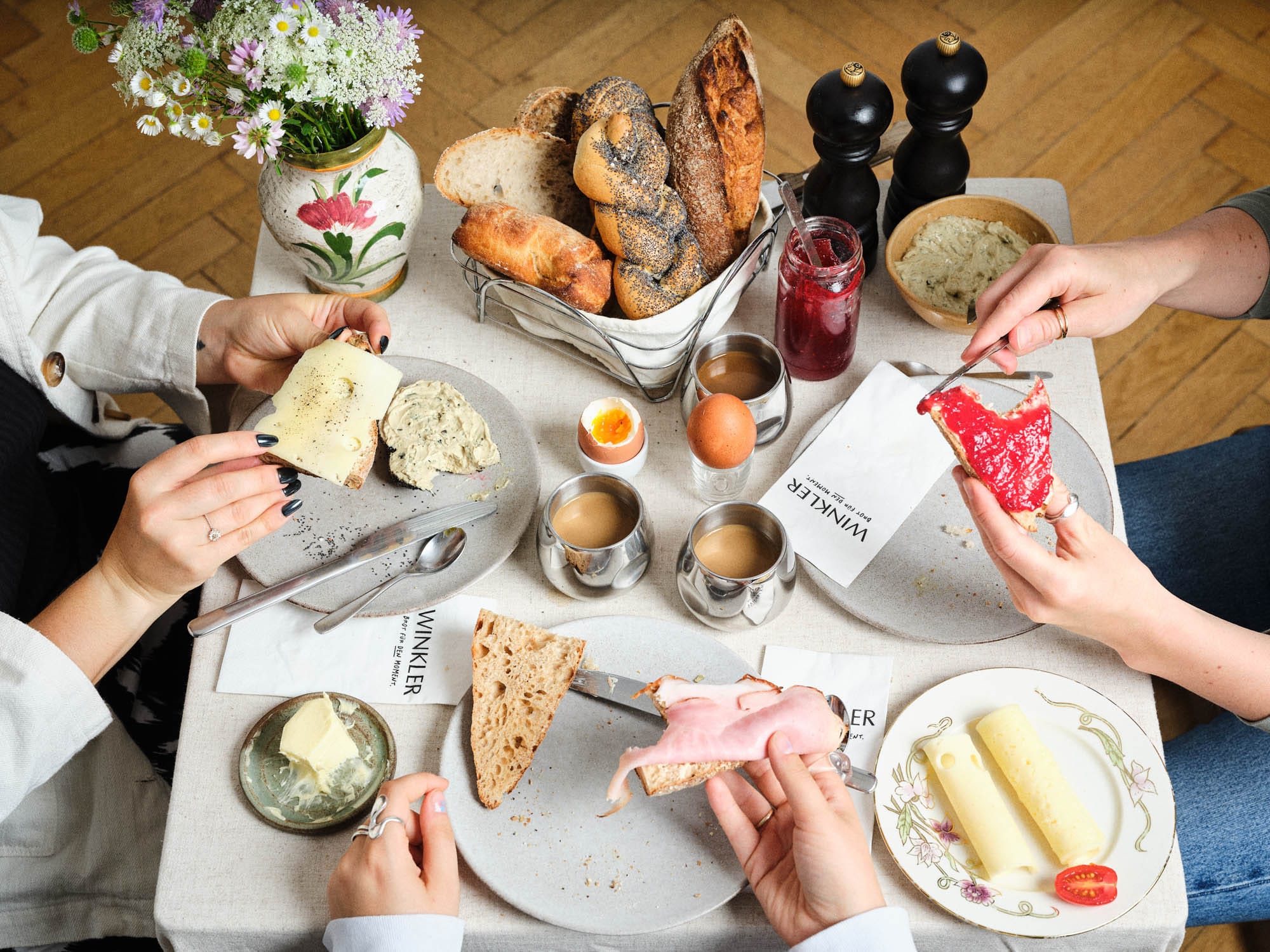 Bäckerei Winkler Frühstückstisch mit Gebäck und Händen die Besteck halten.